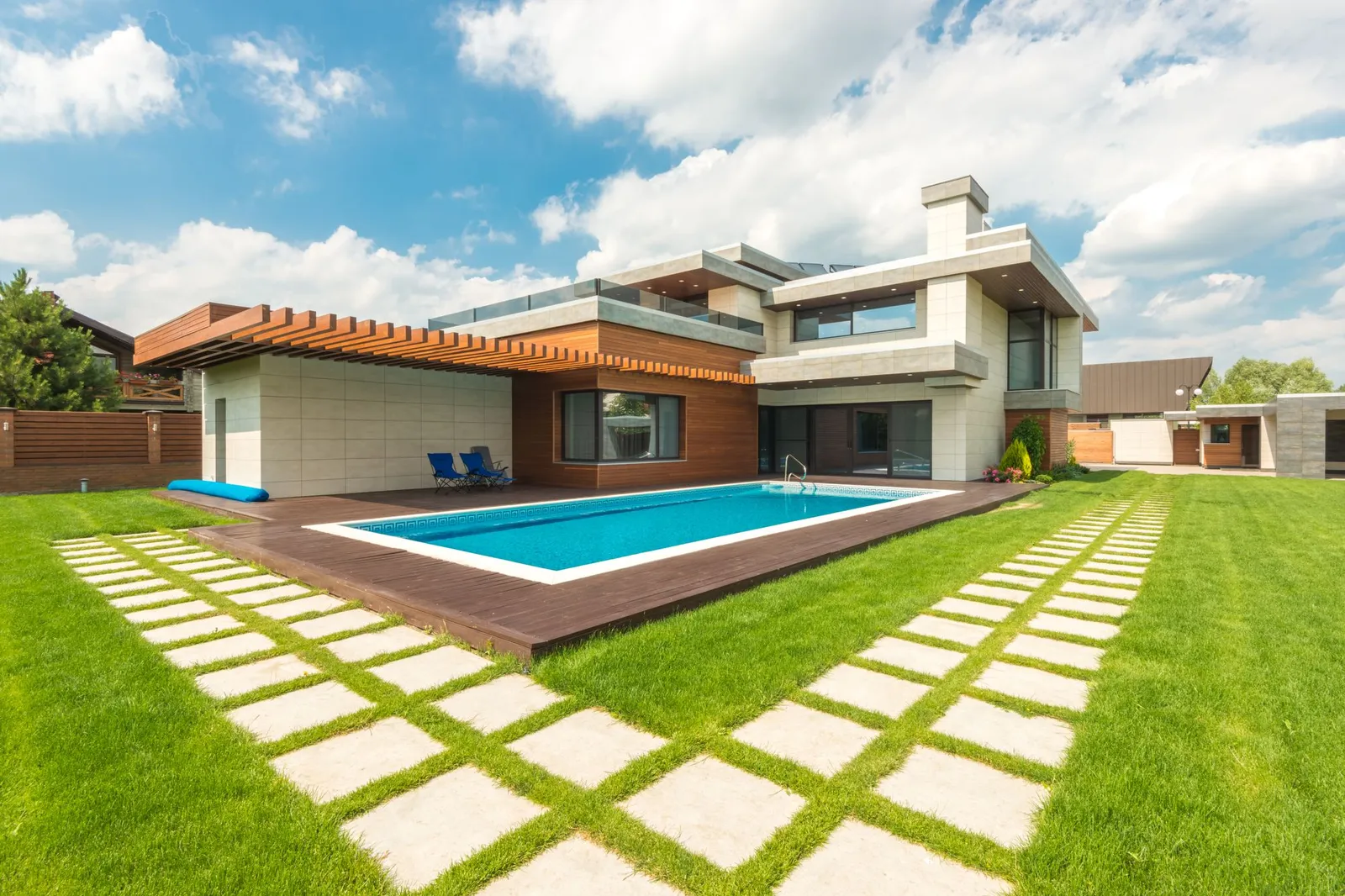 Backyard swimming pool beside a modern house under a blue sky